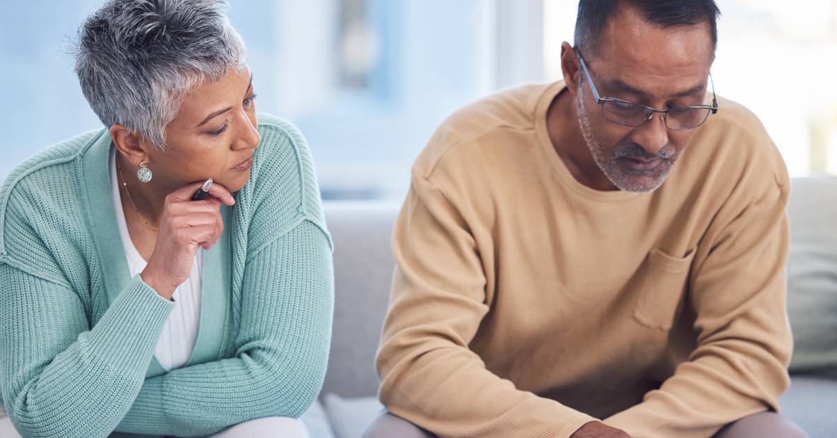 An elderly couple is sitting in the lounge of their house with documents, planning their tax and home budget with the help of a laptop and calculator.