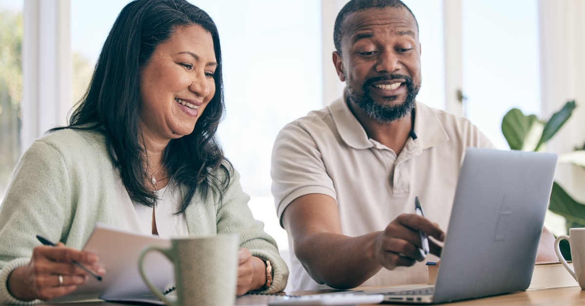 african american couple sitting at table reviewing bills while using laptop at home