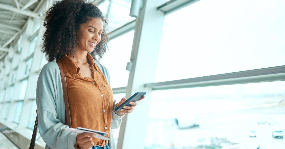 a woman gracefully walking through the airport with her luggage and expertly checking social media on phone.