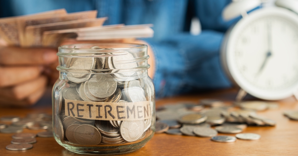 coins placed in glass jar with retirement label on table with man counting bank notes in background
