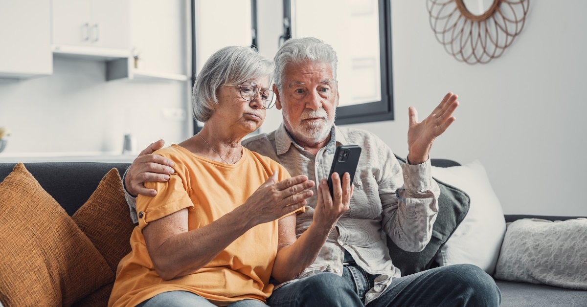 senior couple sitting at home stressing over bills while using smartphone