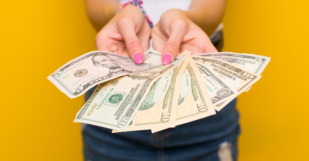 woman having pink nail polish showing bank notes in hand over yellow background