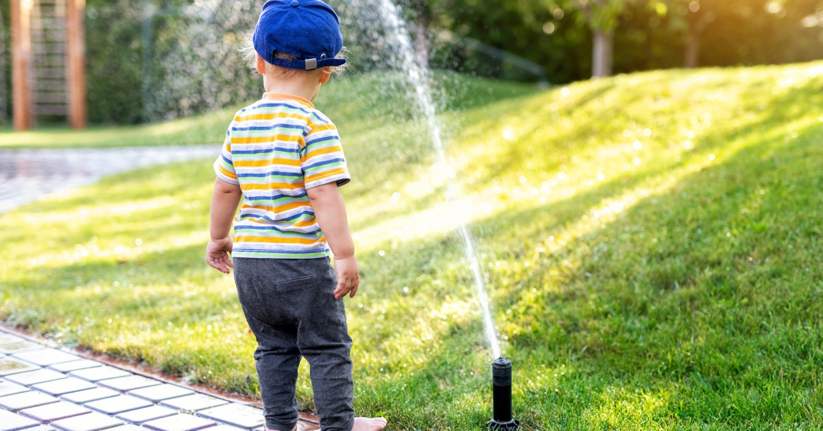 Toddler standing beside sprinkler