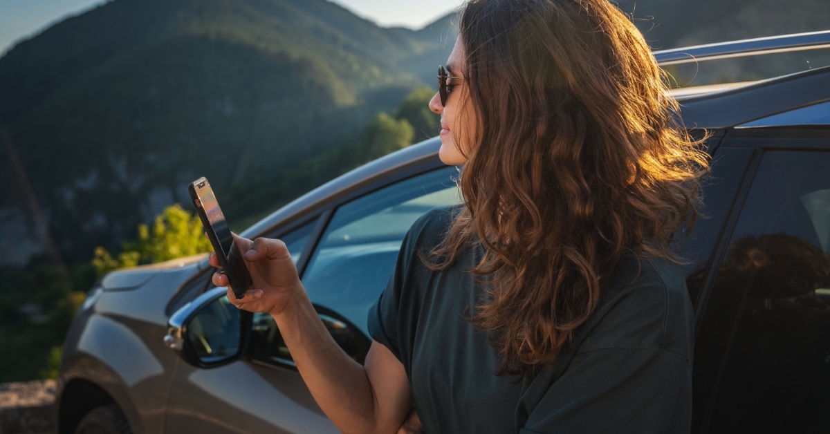 Woman standing besides car using smartphone