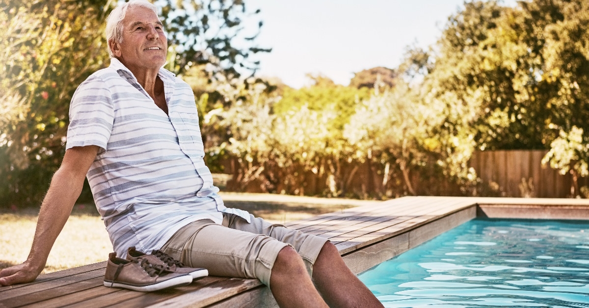 A senior man is sitting by a swimming pool.