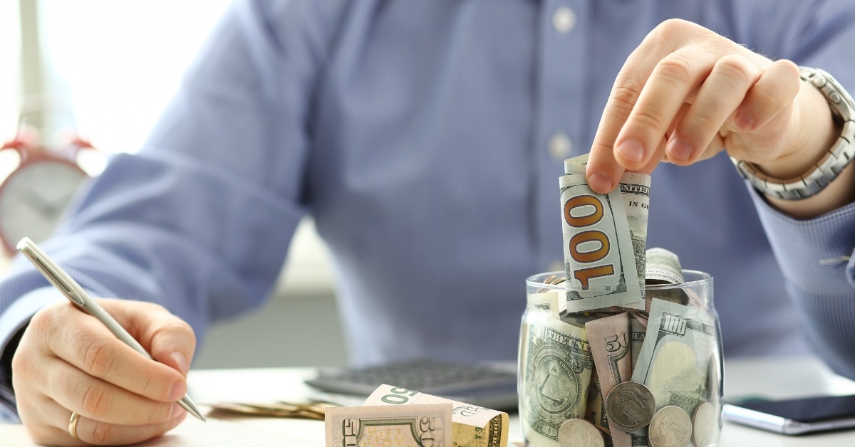 man depositing money in glass jar