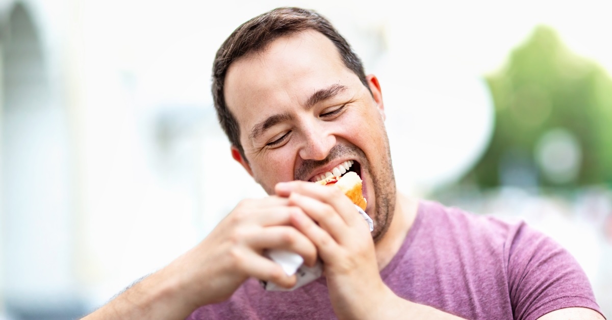 man biting hot dog in street