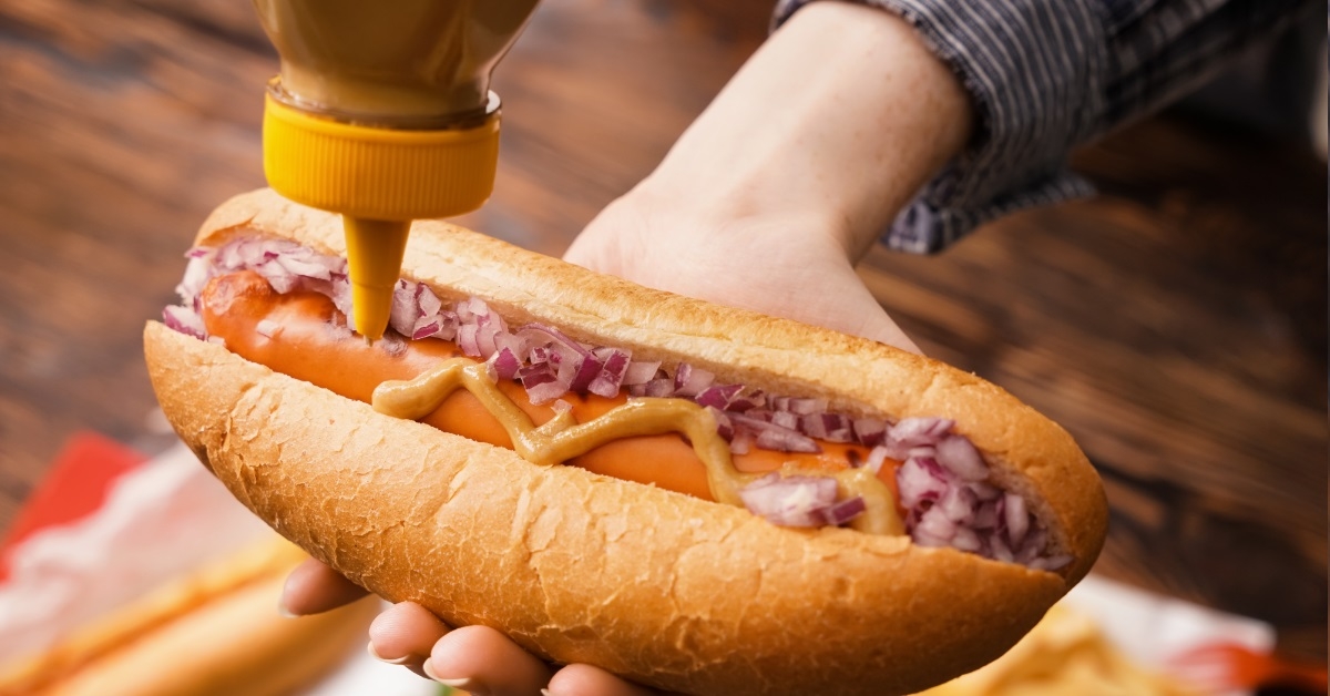woman squeezing mustard on hot dog