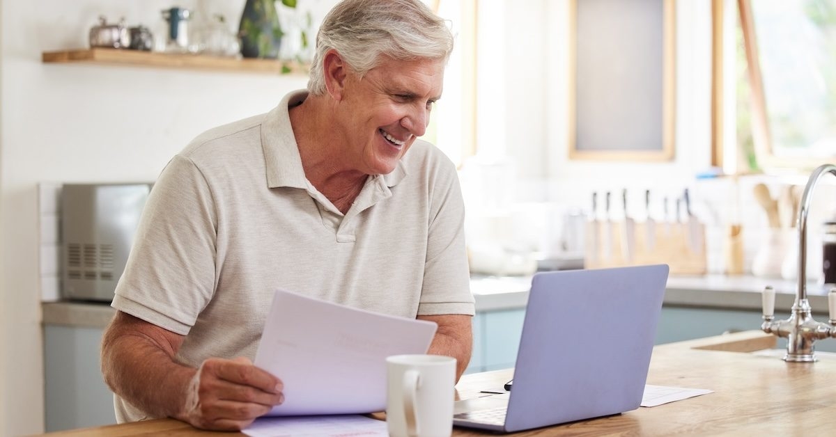 An older man sits in front of a laptop