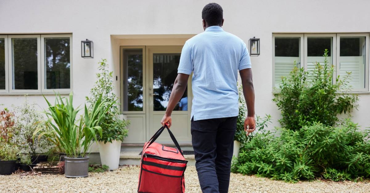 A food delivery driver with a package in hand about to drop off at a home.