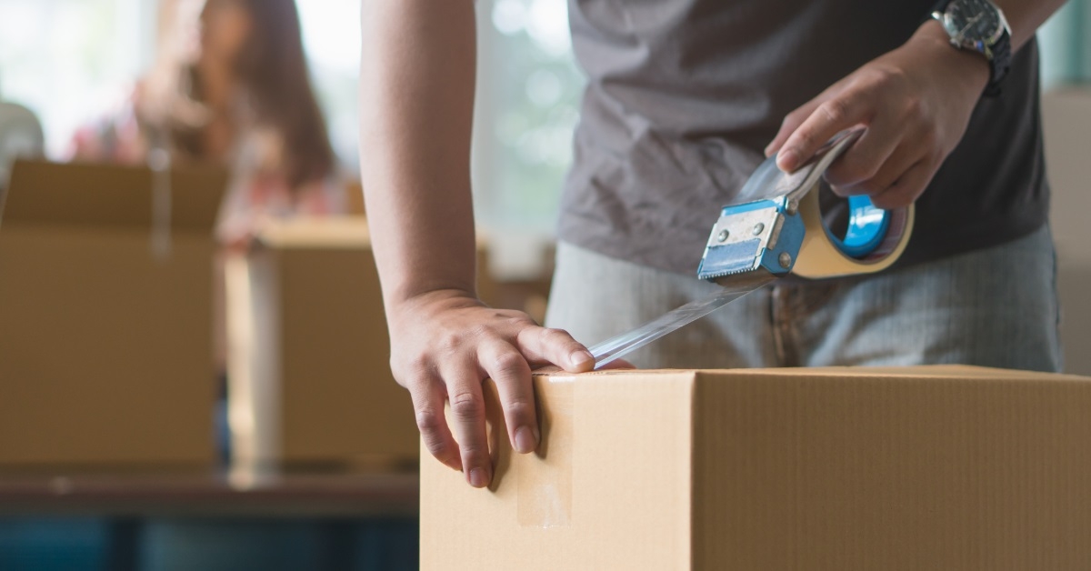man packing moving box with tape