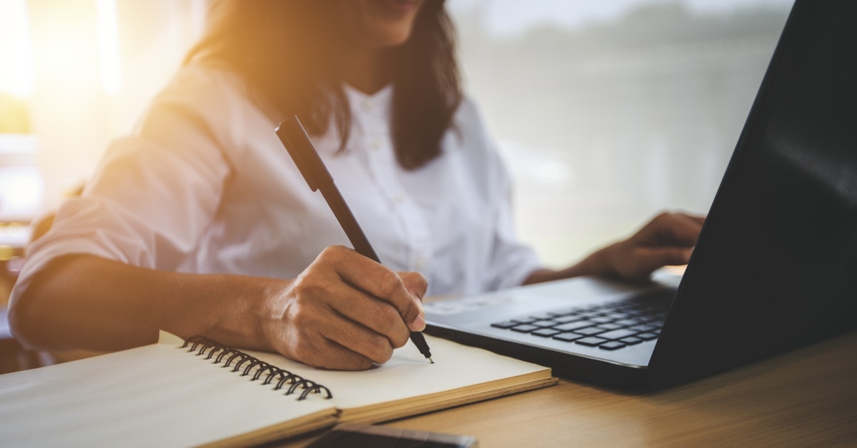 woman writing while attending online class