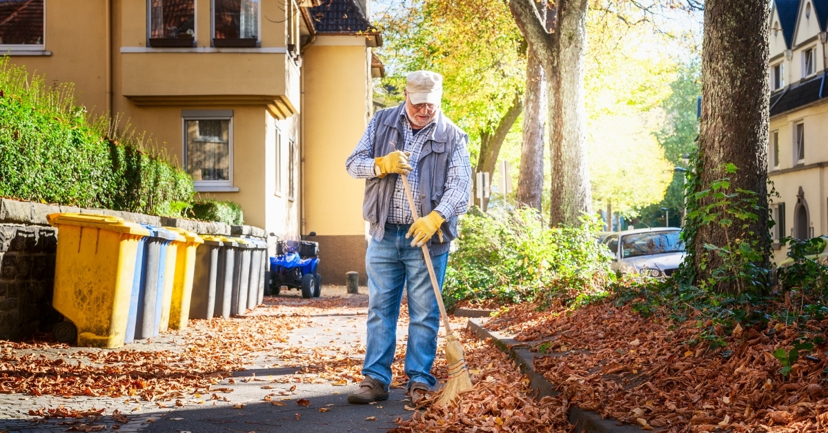 Senior sweeping autumn leaves.