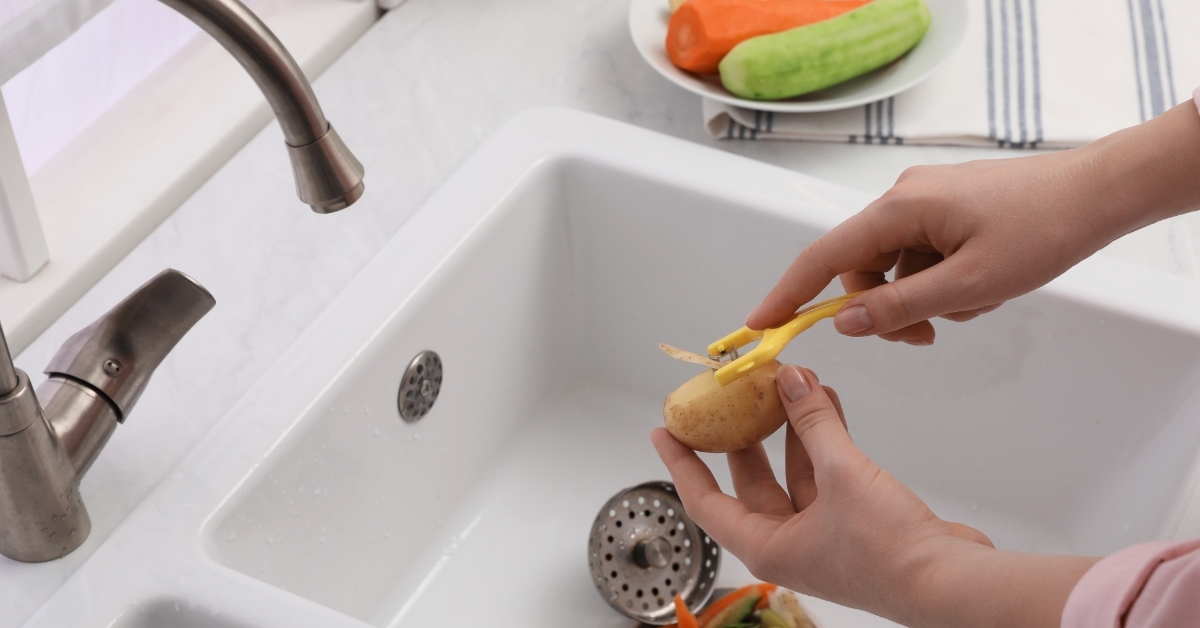 Woman peeling potato over kitchen sink