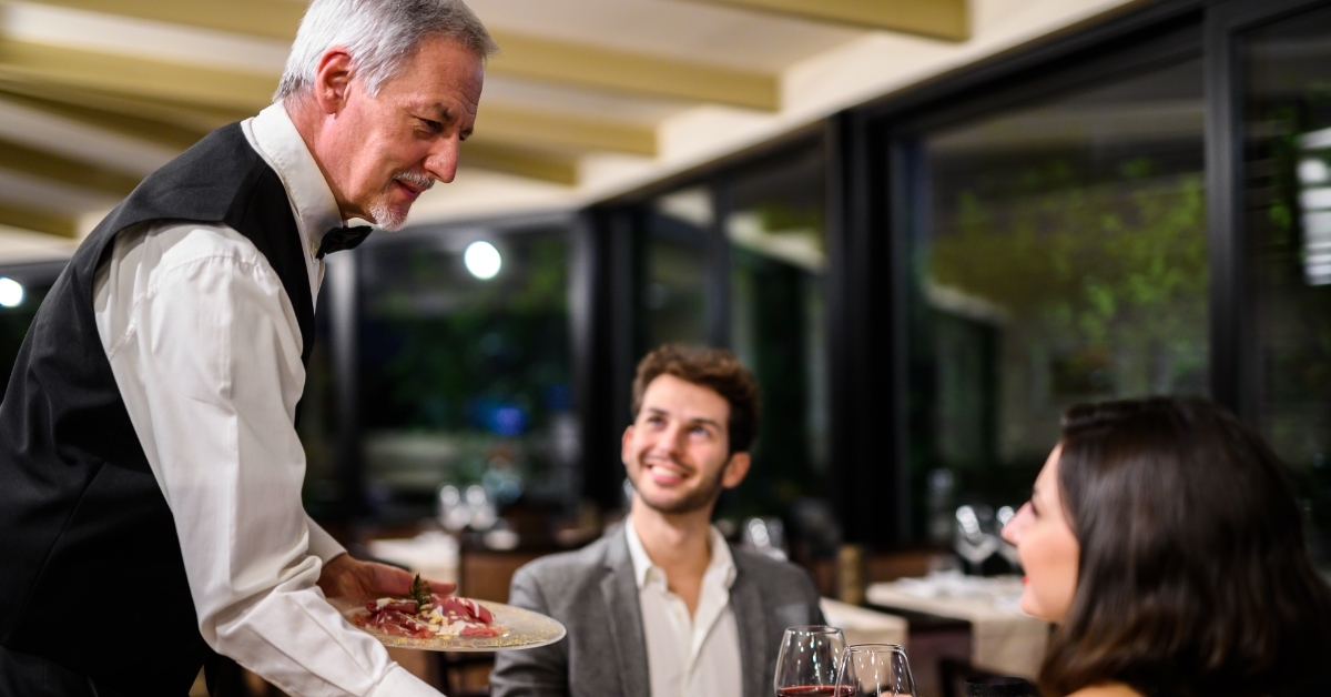 senior waiter serving couple at restaurant
