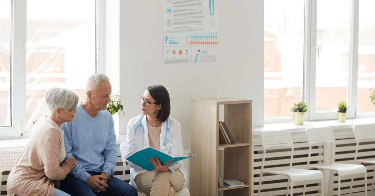female doctor talking to senior couple while sitting in reception area of clinic