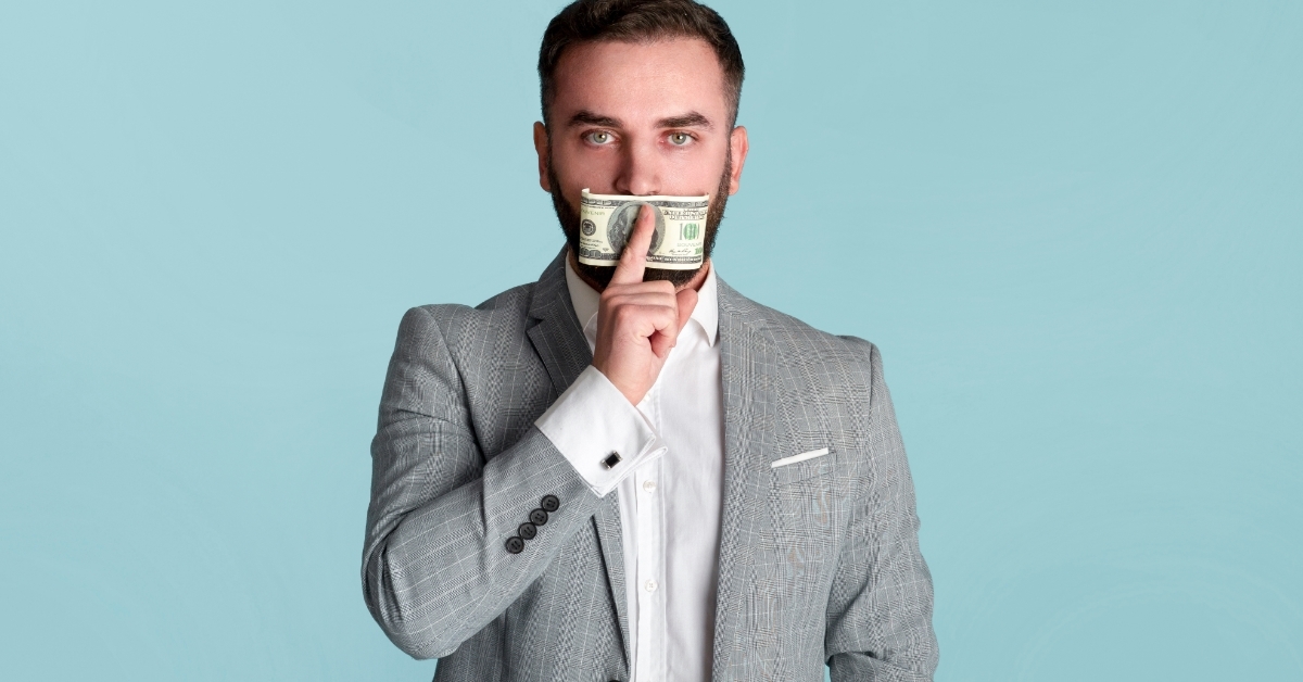 businessman covering mouth with hundred dollar bill