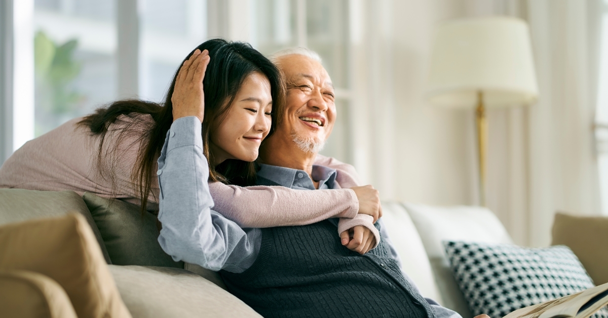 happy asian daughter hugging father on couch