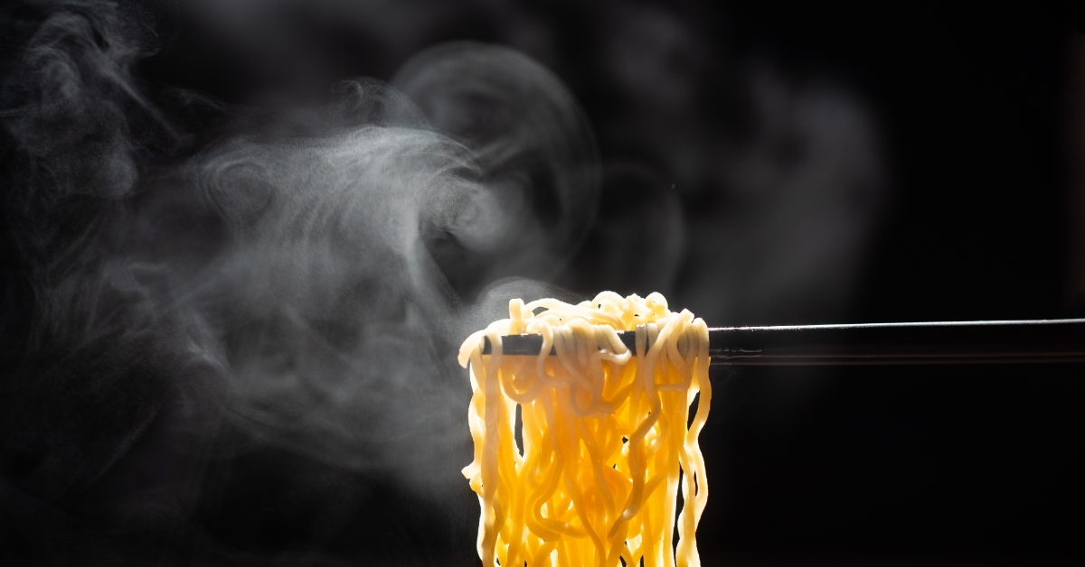 Chopsticks holding steamed noodles over black background