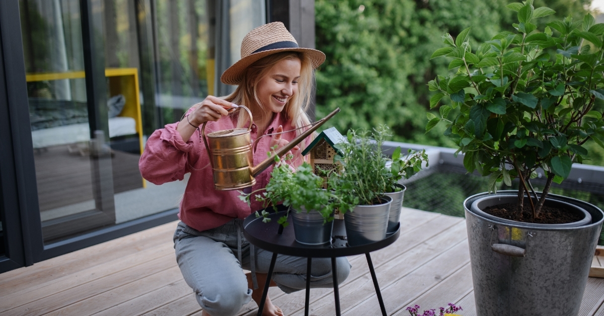 young woman watering herbs on terrace