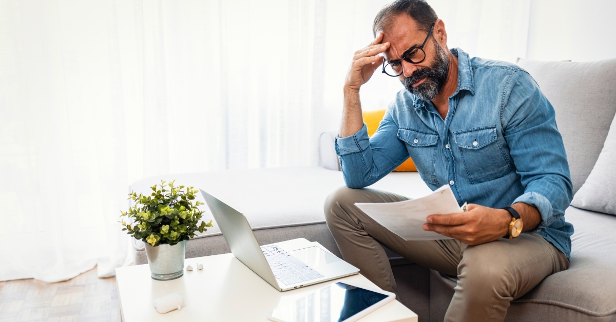 confused senior man holding bills at home