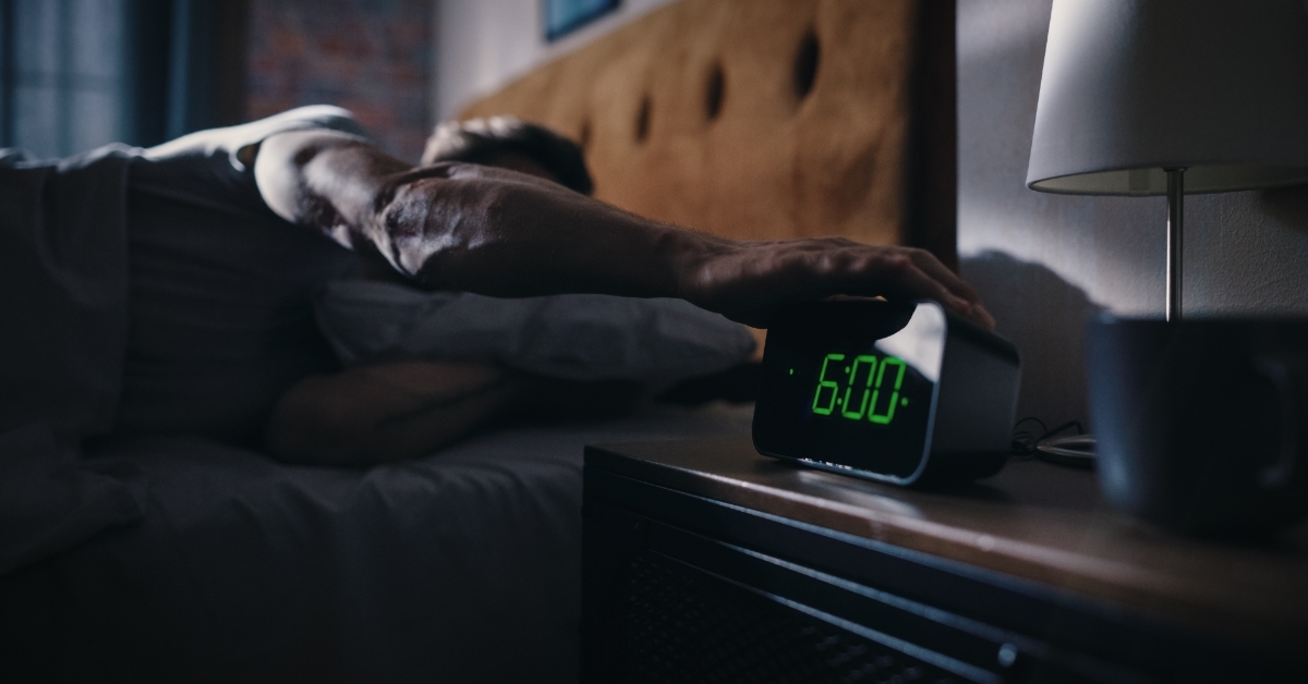 man turning off alarm from bed