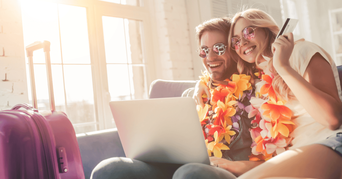 A man and woman wear leis and use a laptop to book their tickets.