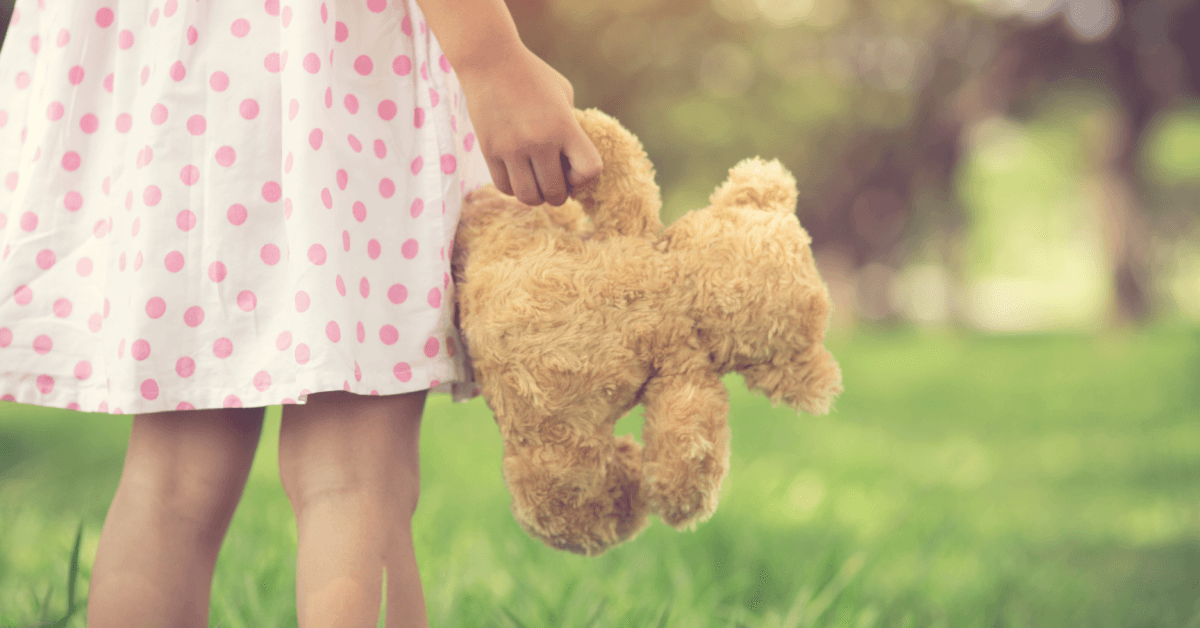 Girl standing holding a brown furry teddy bear.