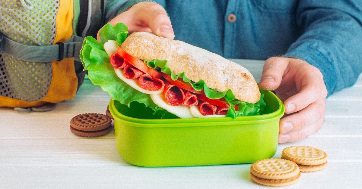 Hands getting a sandwich out of green lunchbox.