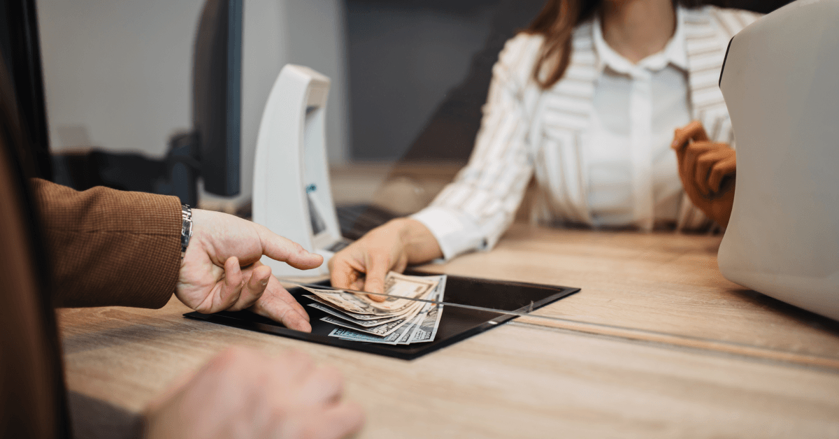 A bank teller hands cash to a customer through a window. 