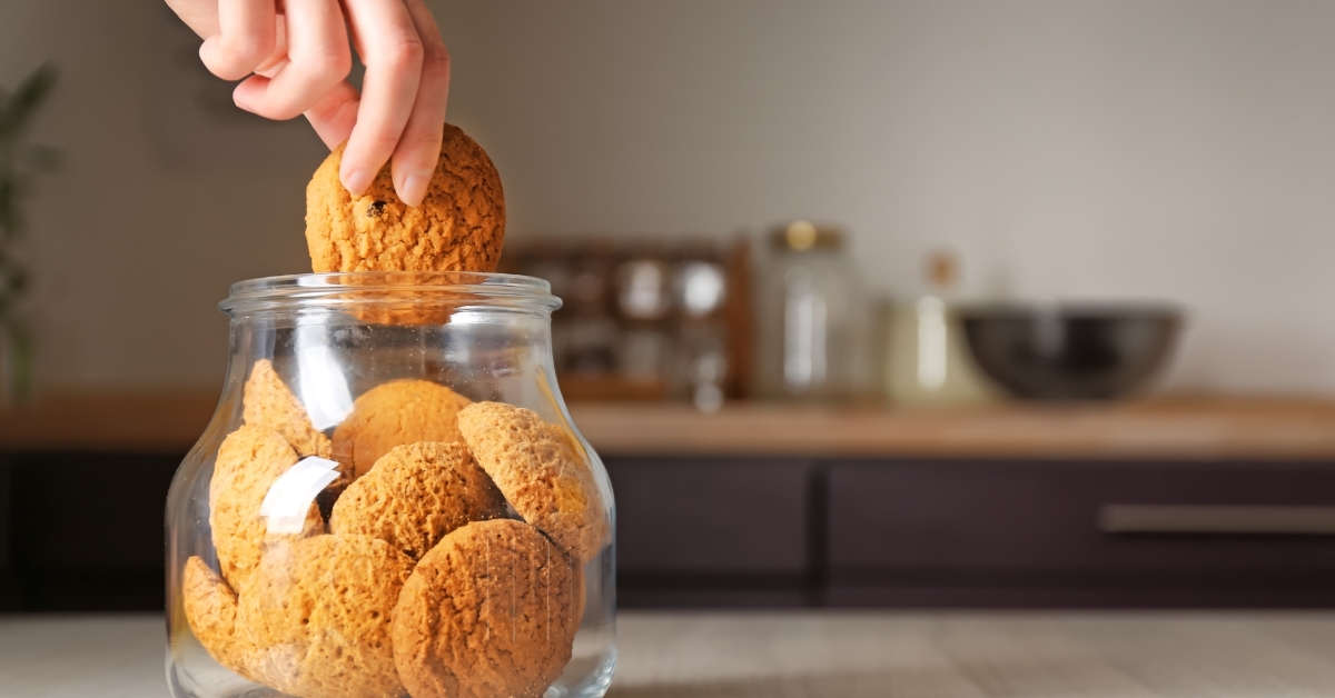 Woman taking oatmeal cookie from jar
