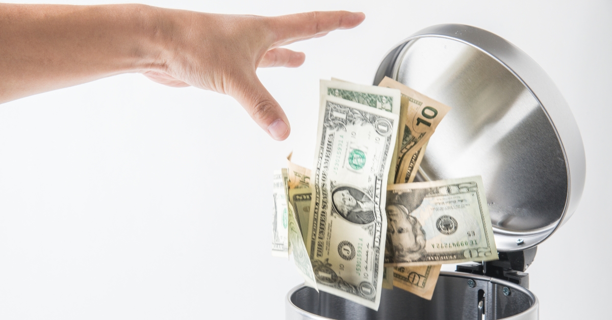 man throwing away dollar in trashcan