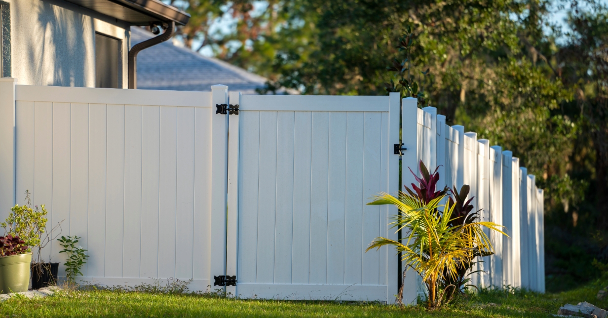 White vinyl picket fence on green lawn surrounding property grounds for backyard protection and privacy 