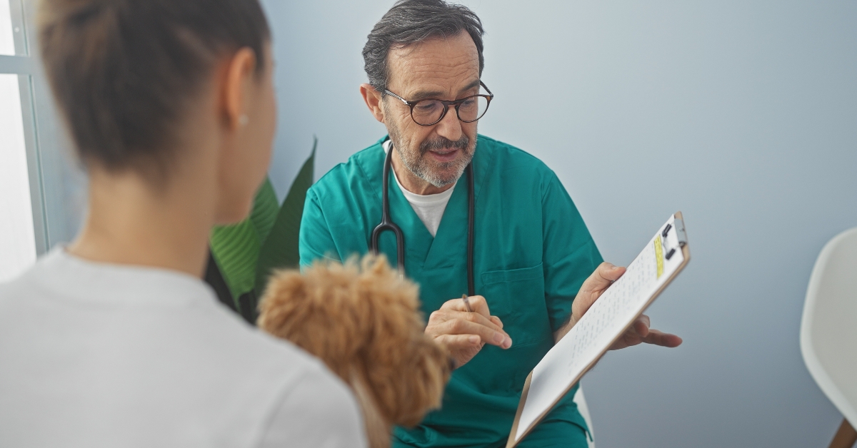 man in scrubs consults with a female client holding a poodle