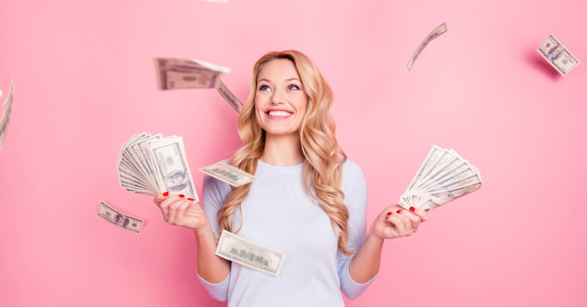 successful lucky cheerful girl standing under shower from money