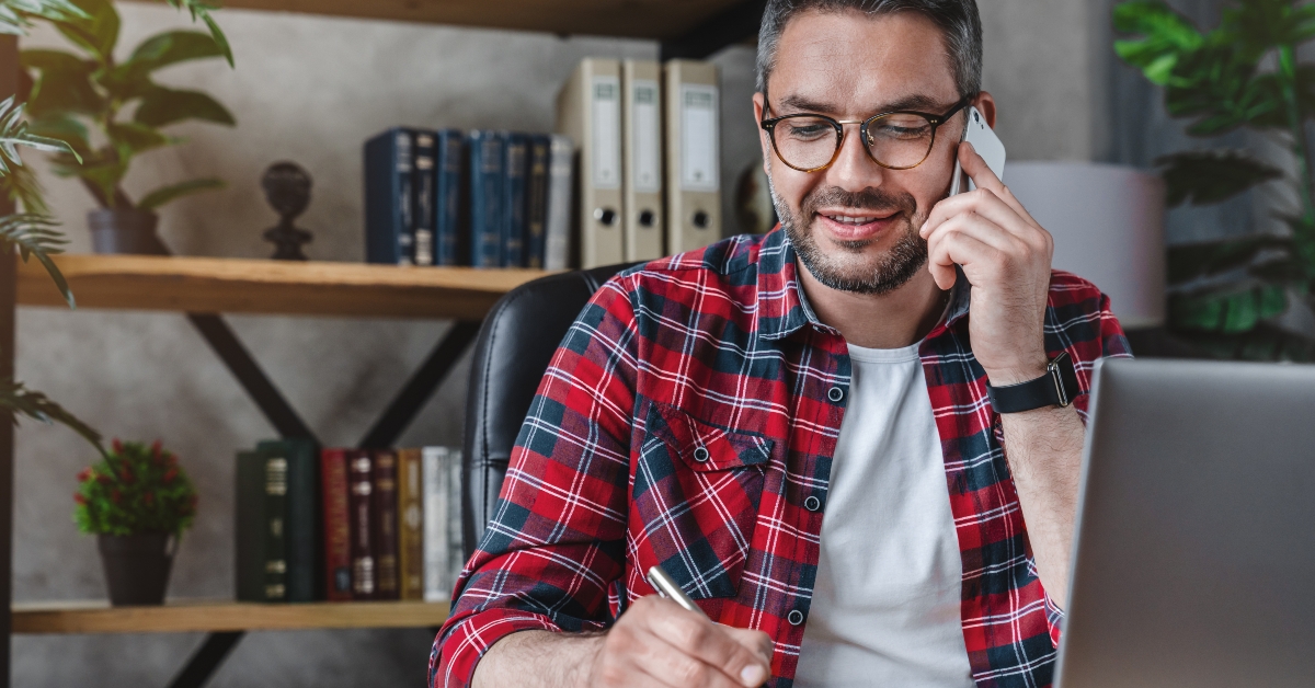 man writing notes while making phone call 