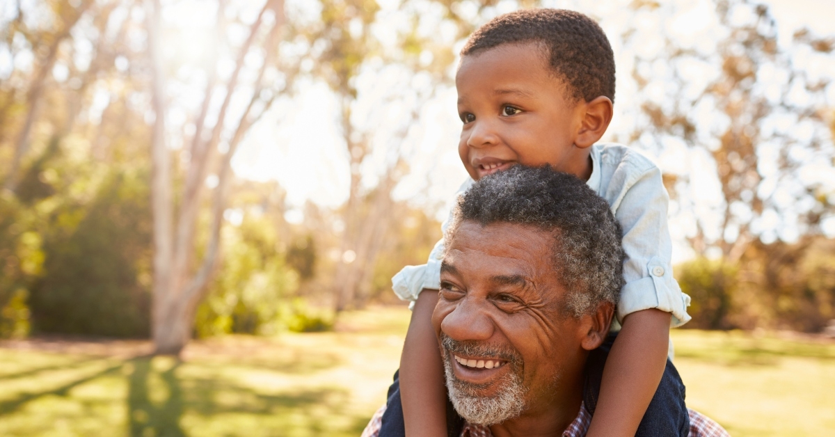 grandfather carries grandson on shoulder during walk in park