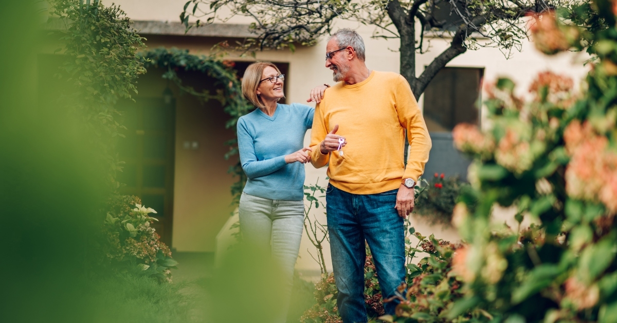 senior couple holding keys and standing outside their new home