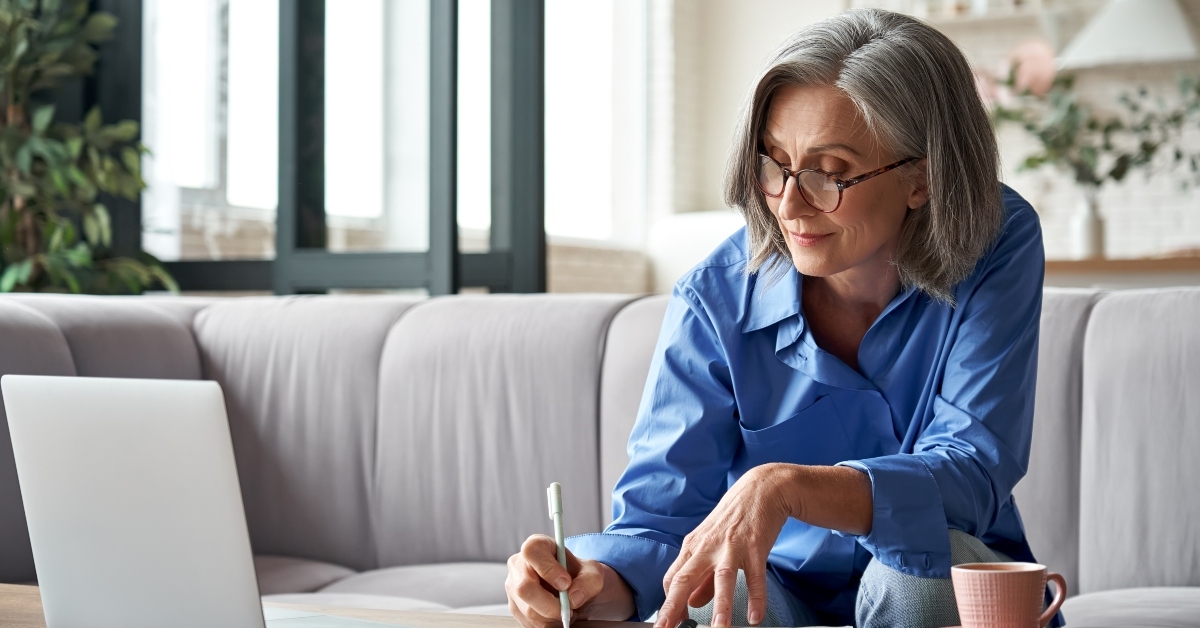 old woman working from home using laptop and taking notes