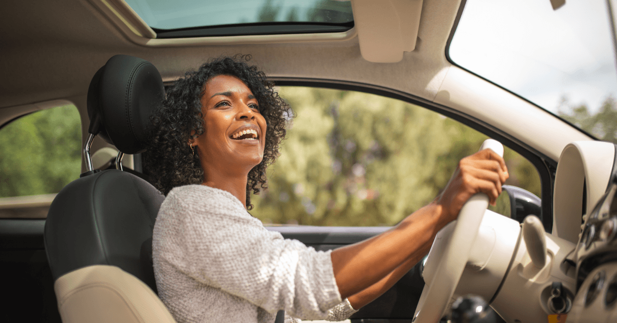 A woman grips the steering wheel and smiles while driving her car.