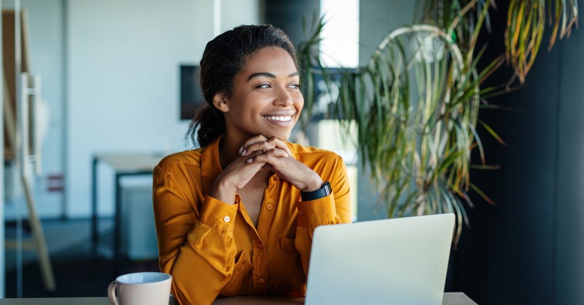 businesswoman sitting at desk thinking while working on laptop 
