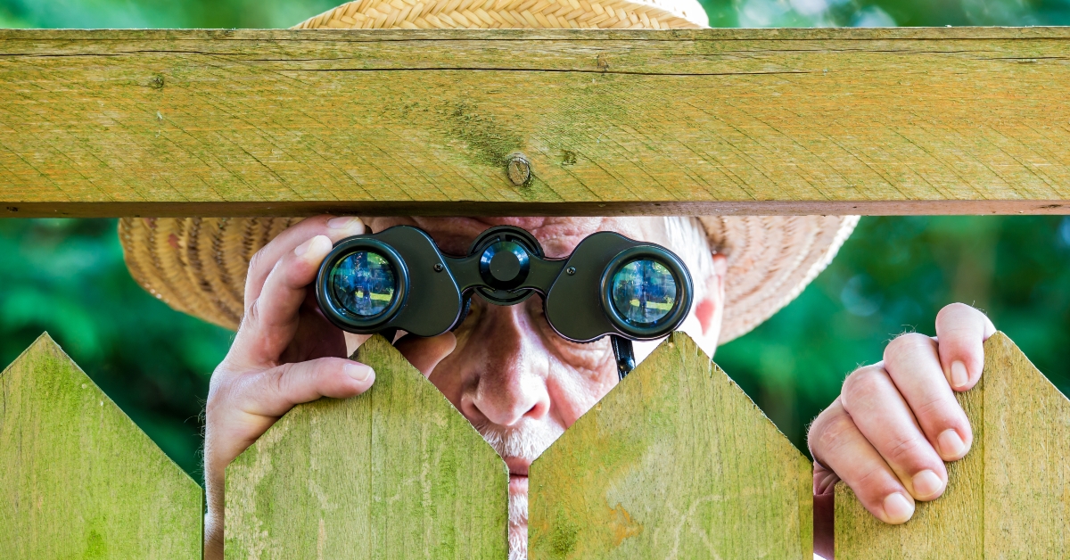 a curious neighbor stands behind a fence