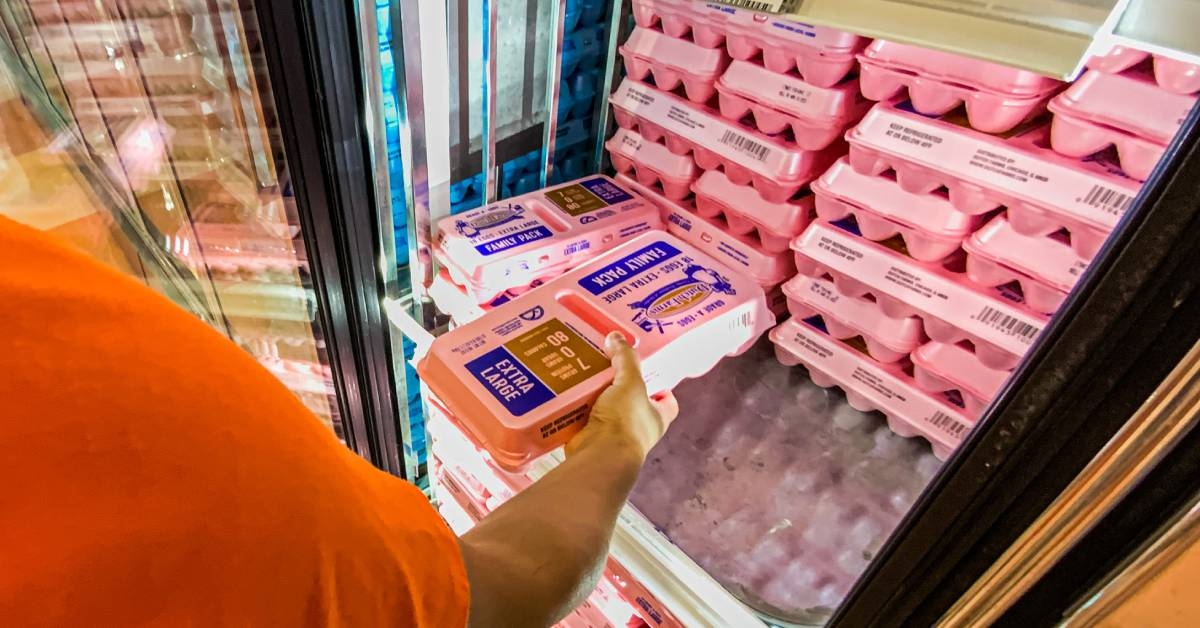 woman shopping in a grocery store grabbing a polystyrene foam carton of eggs from refrigerator