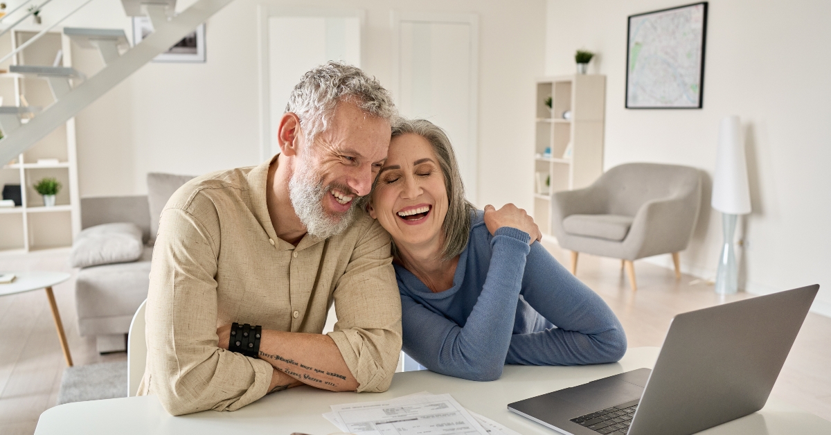 couple laughing sitting at the home table with laptop