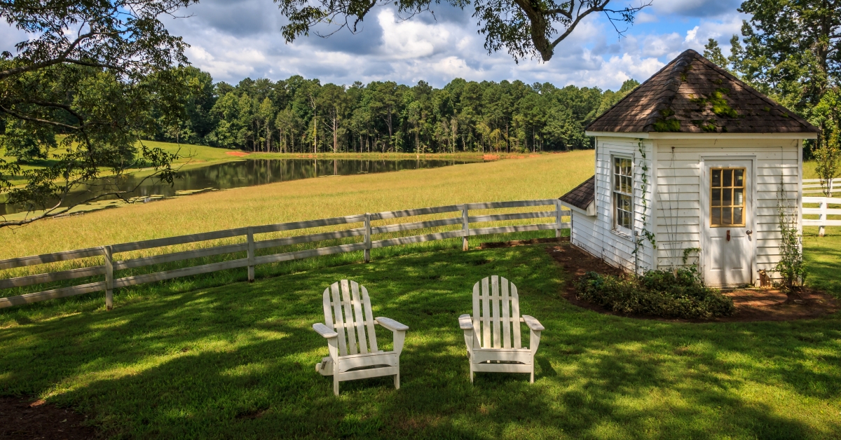 Adirondack chairs sit on a lawn in front of a white fence