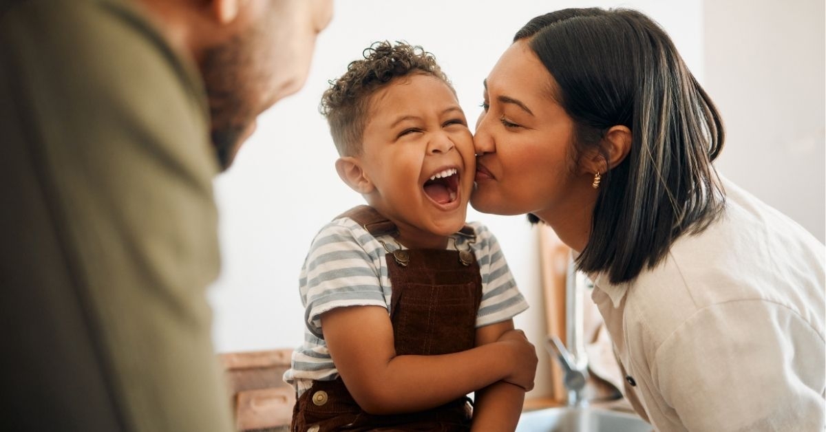 Happy boy getting a kiss by caring mother, bonding and laughing during family time at home.