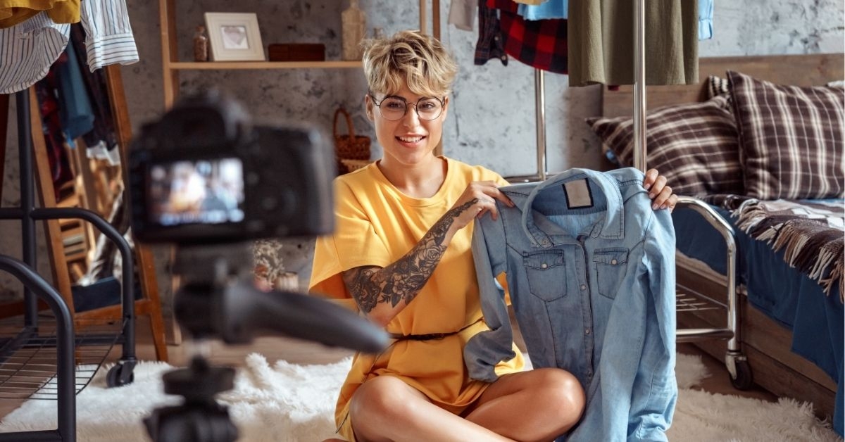 Fashion Blogger. Young woman influencer in glasses sitting on carpet at stylish apartment recording vlog on camera 