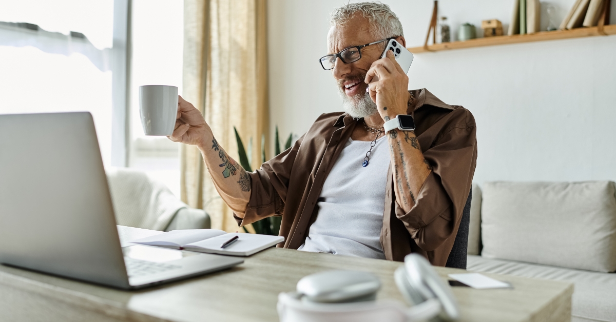 man with grey hair and tattoos smiles while working remotely