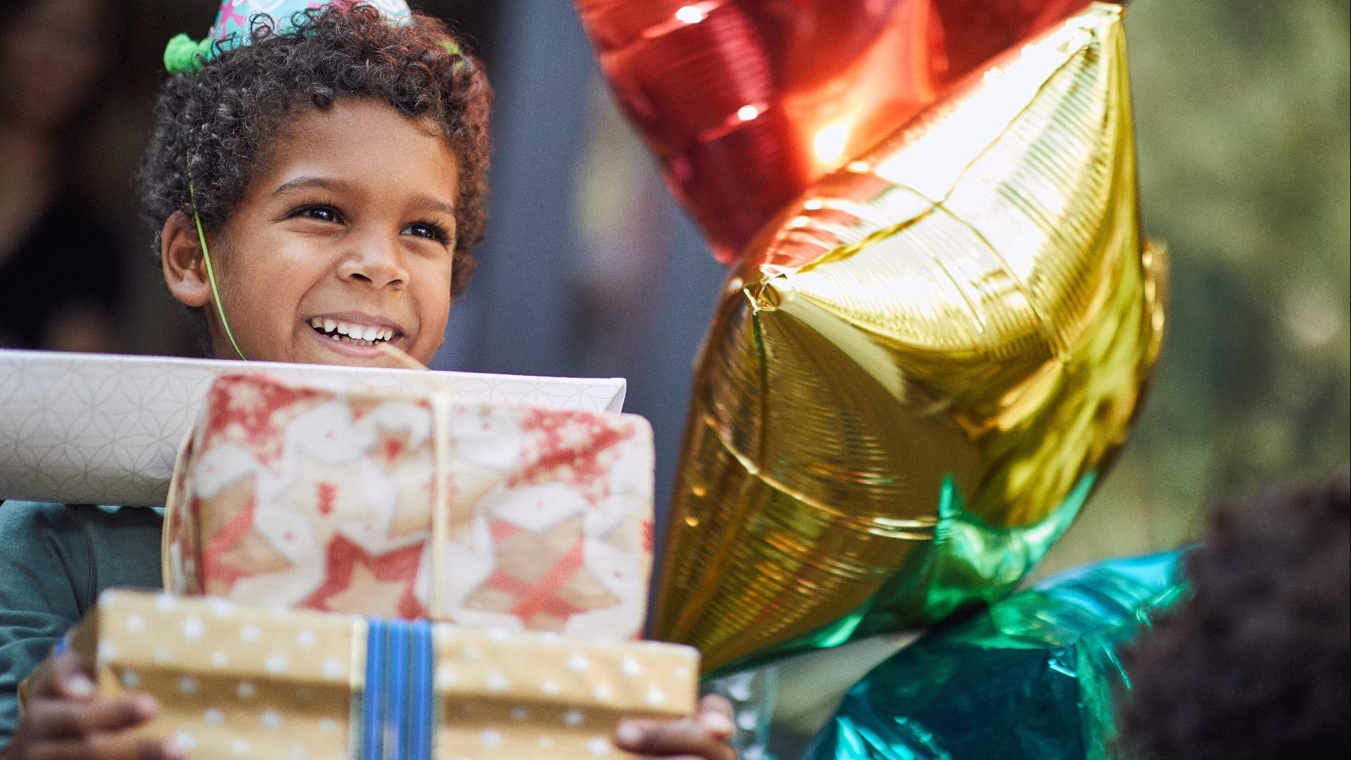 Little boy in birthday cap holding pile of birthday presents