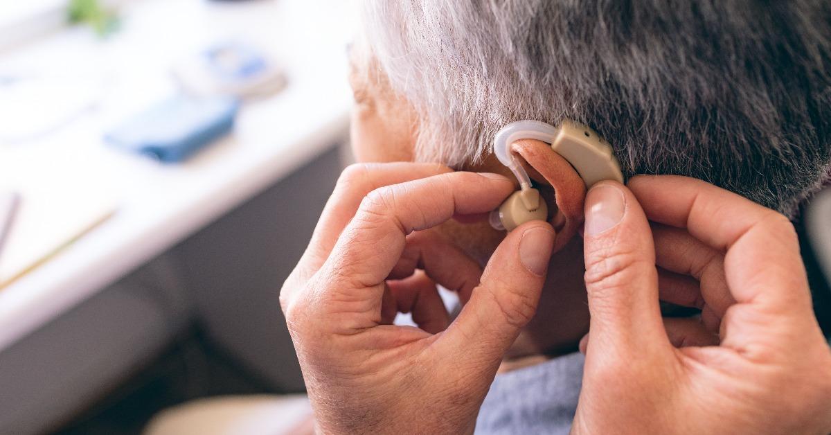 male doctor applying hearing aid to senior woman